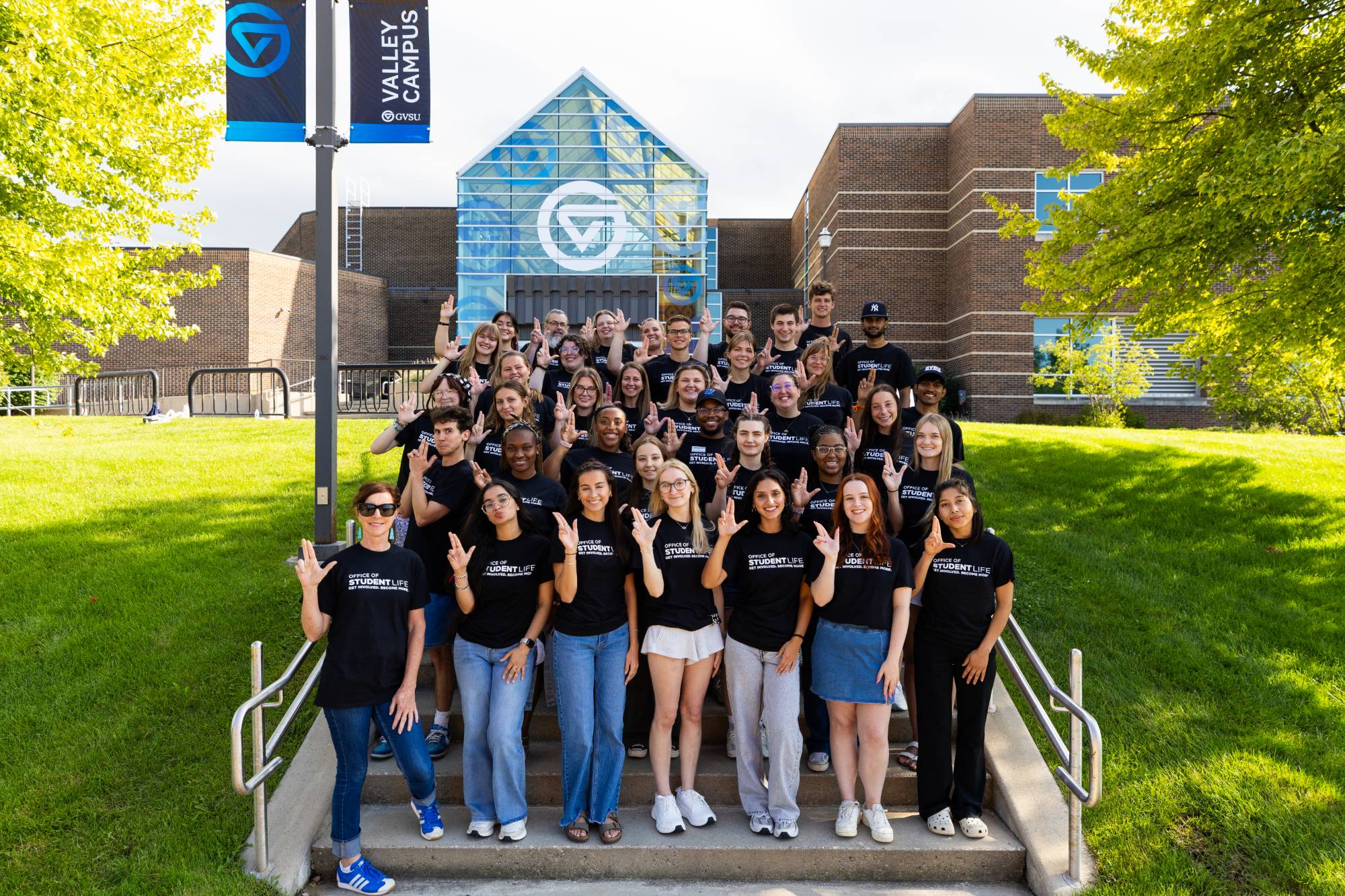 A group of staff wearing black Student Life t-shirts and raising the "anchor up" hand signal